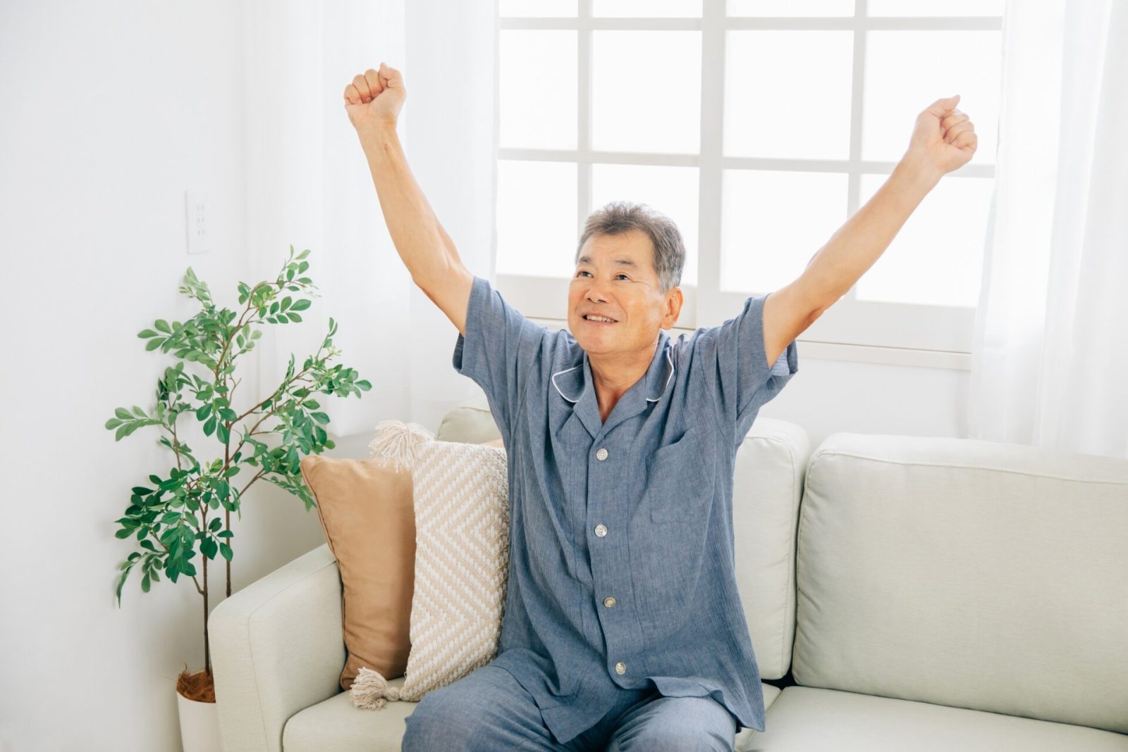 ソファにかけて両手を天井に伸ばしてストレッチしているパジャマ姿の男性