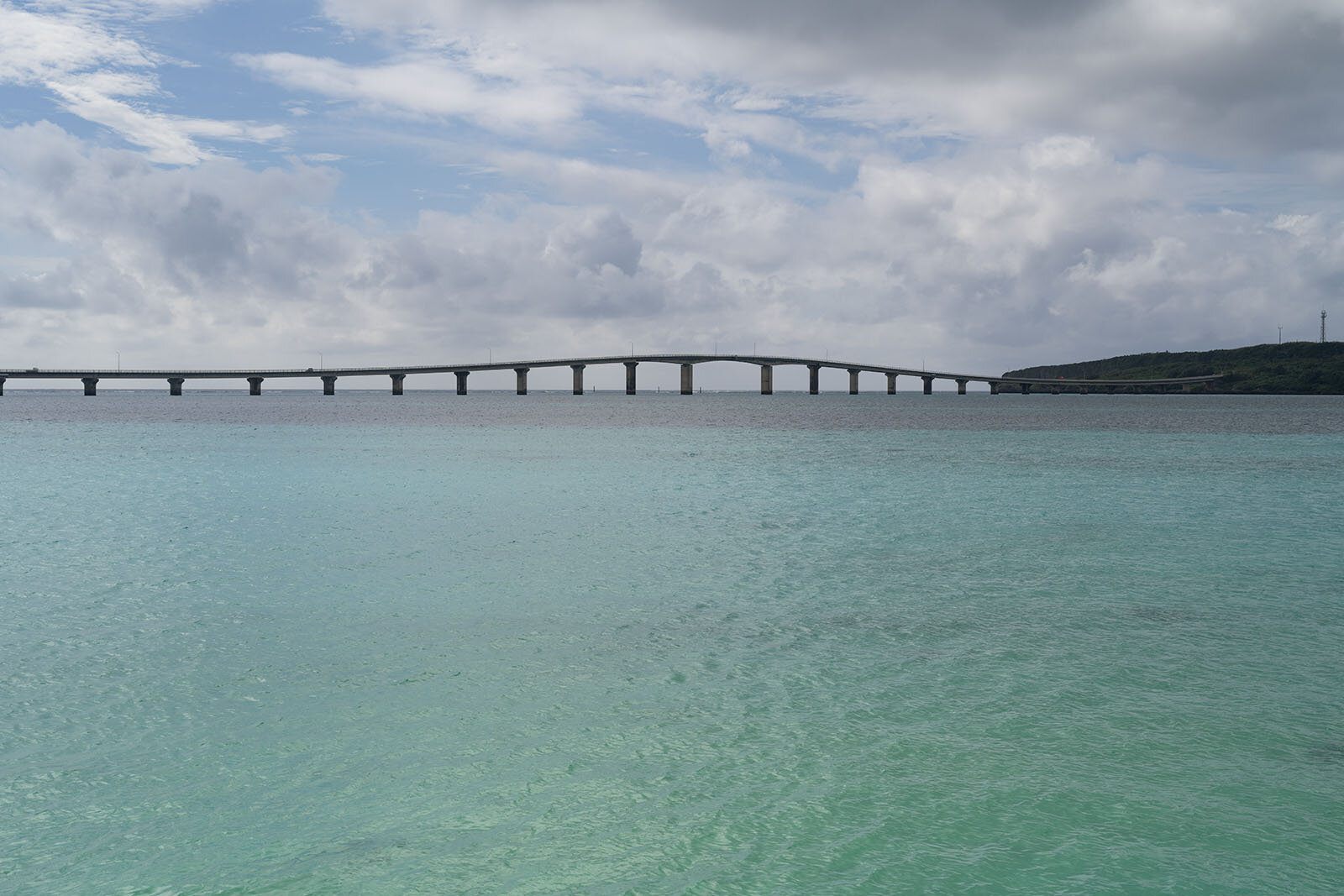 青空、白い雲、透明な碧い海が織りなす海とビーチからの橋の風景