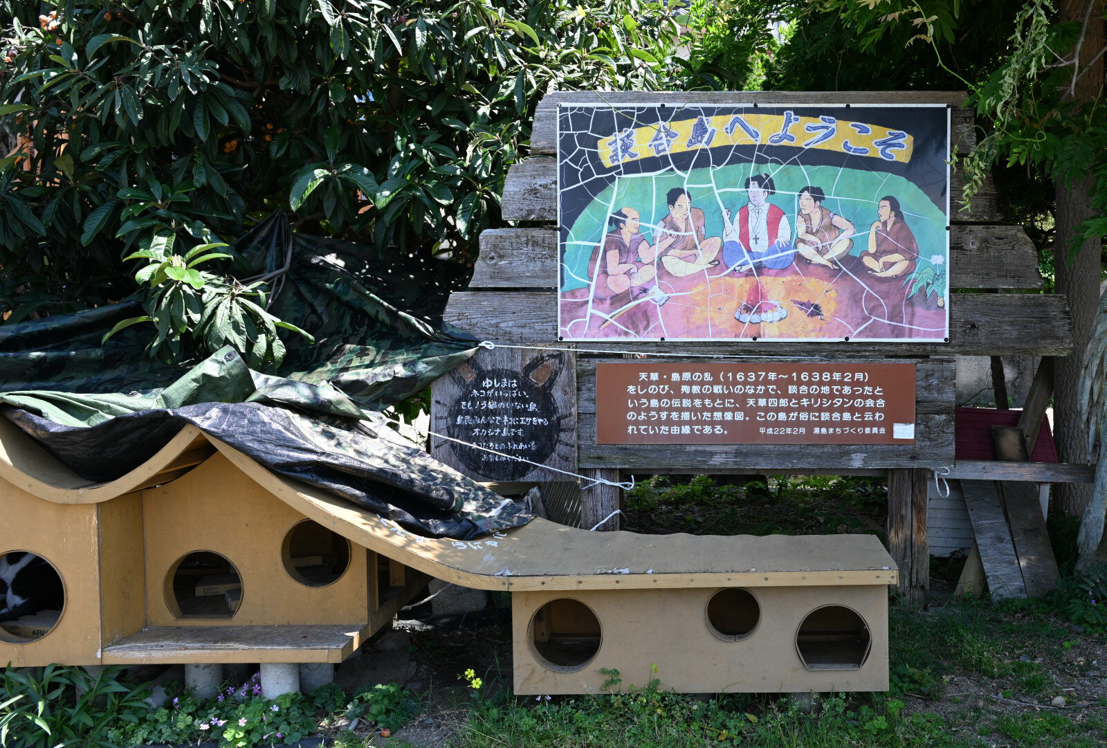 「談合島へようこそ」という看板と、猫が遊ぶ穴あき台が見える