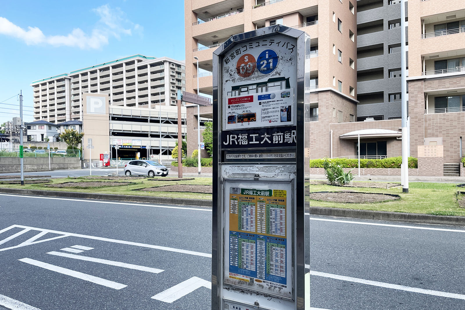 「JR福工大前駅」と書かれたコミュニティバスのバス停看板。背景には道、パーキング、マンションなどが写っている