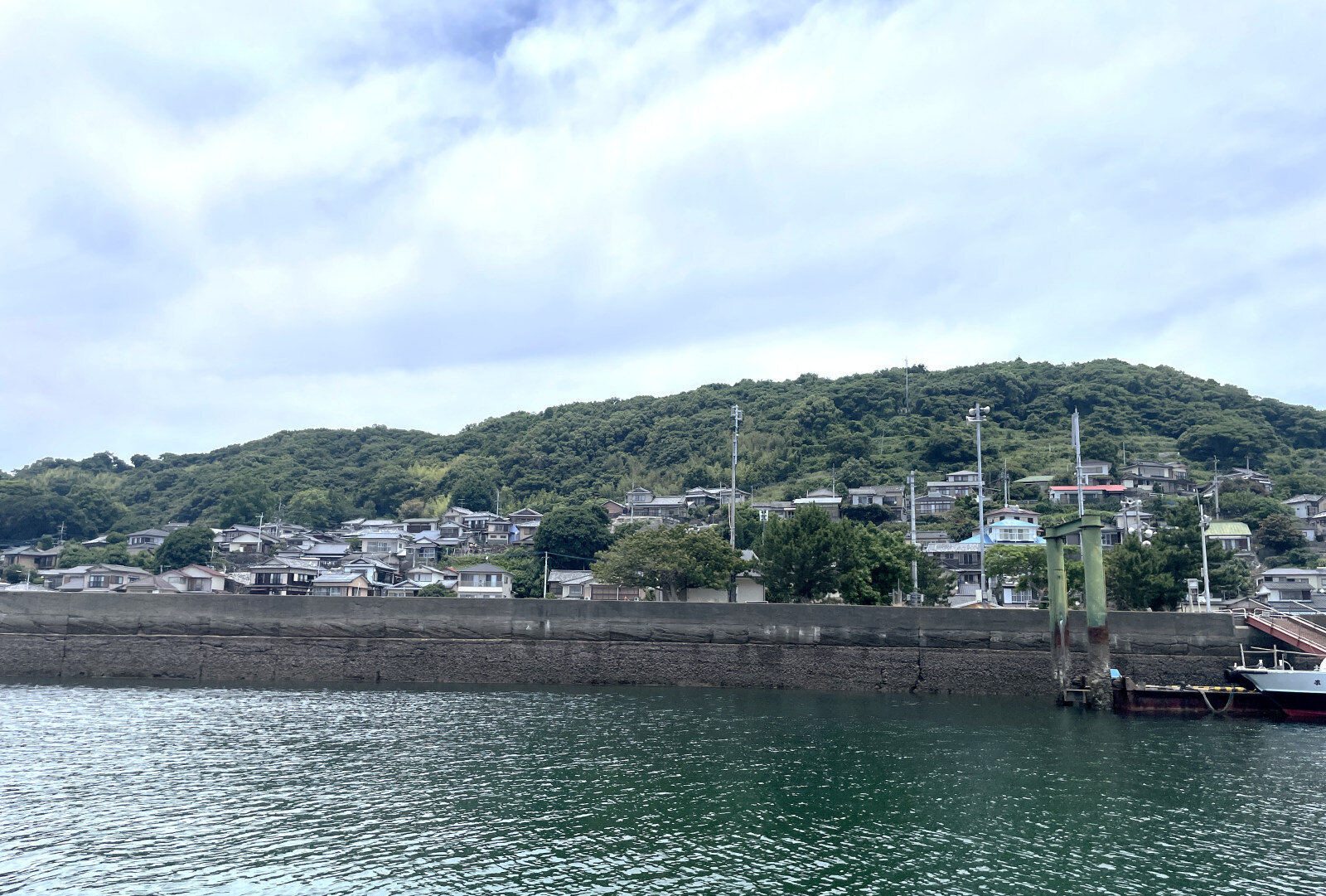 防波堤の向こうに広がる家々と山並み、穏やかな波が静かにその景色を映している