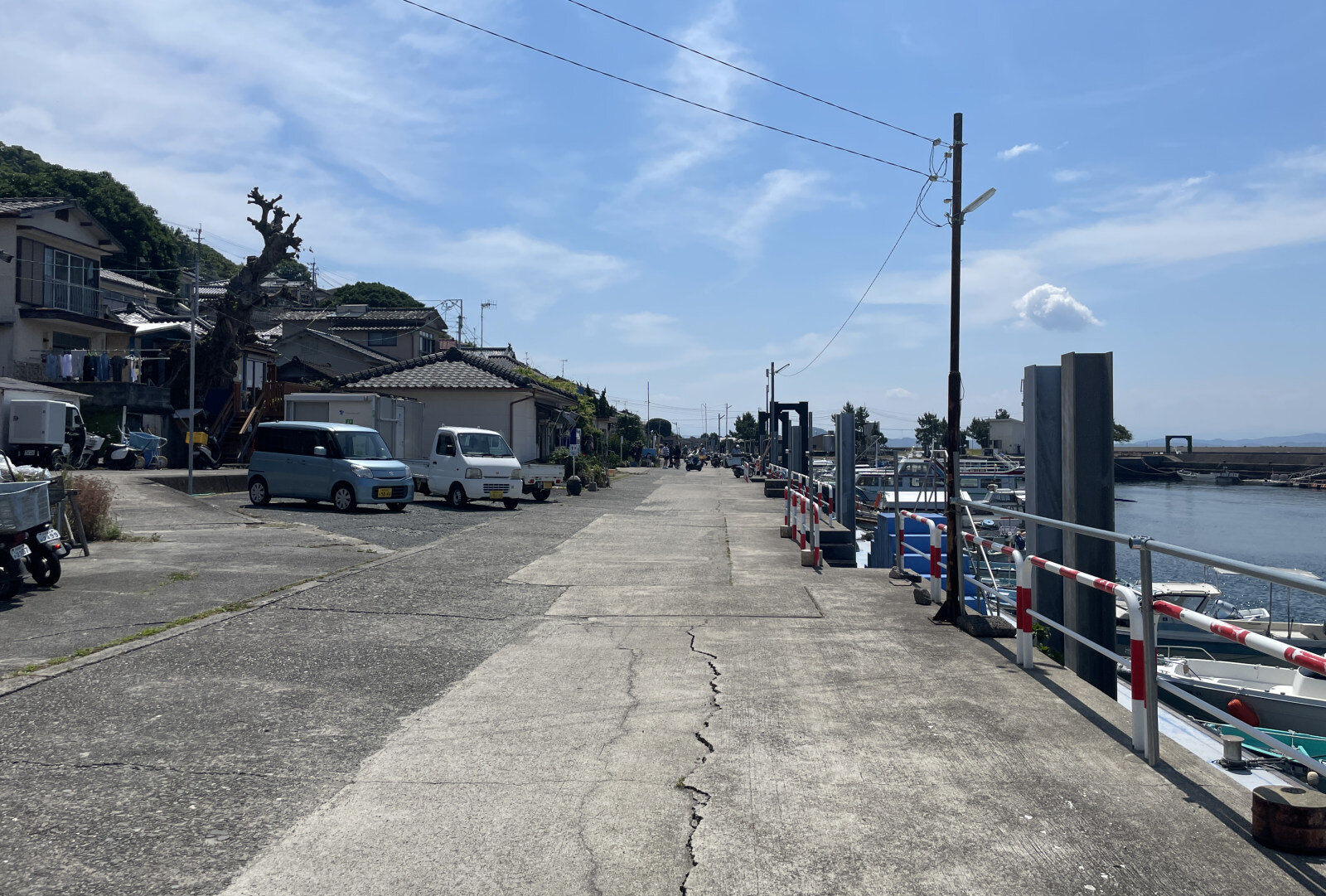 港町の海辺に沿った道の反対側には、家々と停まった車が並び、静かな空気が流れている風景
