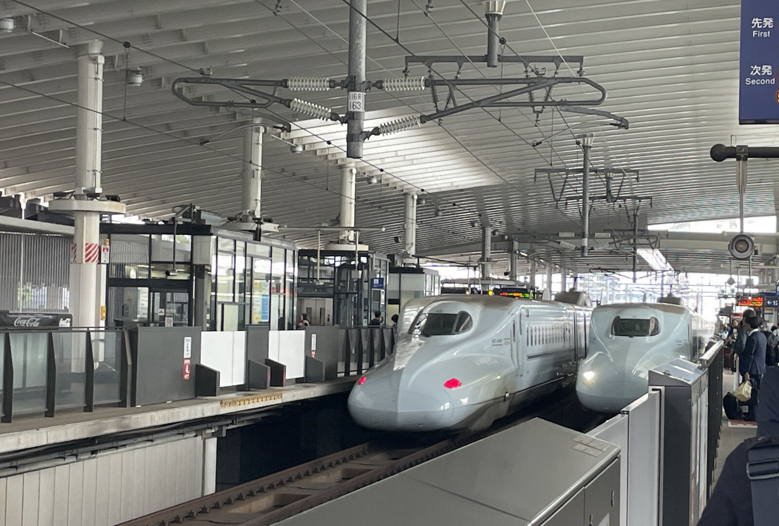 九州新幹線のさくら号が2台、ホームに並んで停まり、乗車を待つ人々が列をつくっている