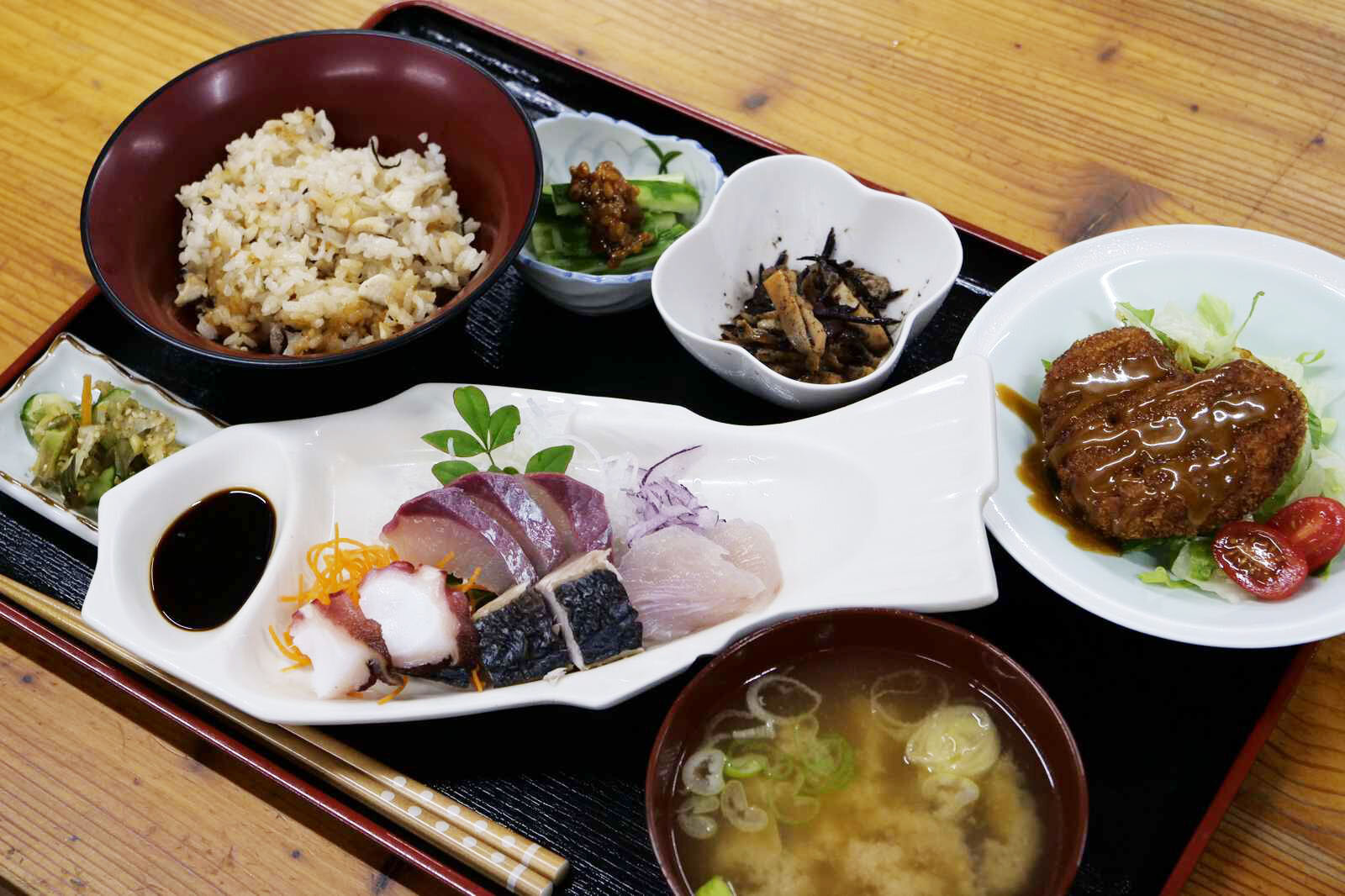 味噌汁、お刺身、炊き込みご飯、お惣菜が整然と並んだ定食セット。お刺身は魚の形をした皿に盛り付けられている