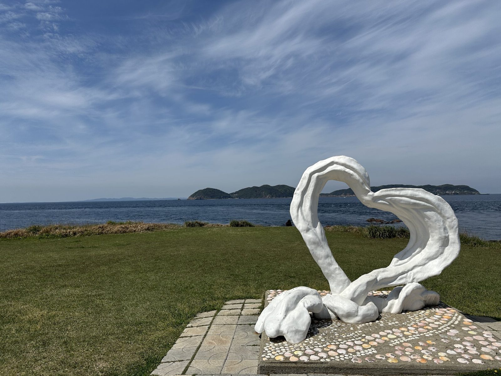 芝生の上に白い石でできたハートの形のモチーフがあります。向こうには海と島が見えます